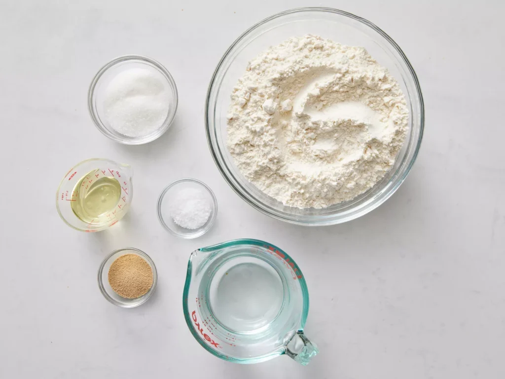 Ingredients for bread machine recipe, including flour, water, yeast, sugar, and salt, arranged on a kitchen countertop